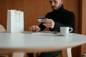 Stylish young male doing online shopping with tablet and credit card in cafe