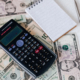 Calculator and notepad placed on usa dollars stack