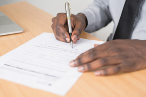 Person holding gray twist pen and white printer paper on brown wooden table